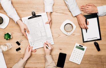 Top view of businesspeople with paperwork, calculator and coffee on table, cropped view